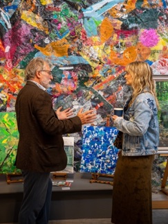 Two visitors in conversation in front of a large, brightly coloured collage mural
