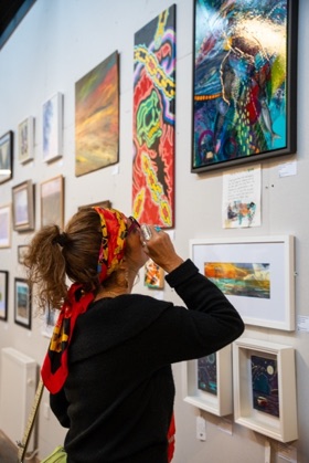 A visitor in a patterned headscarf leaning in to look closely at a painting on the gallery wall