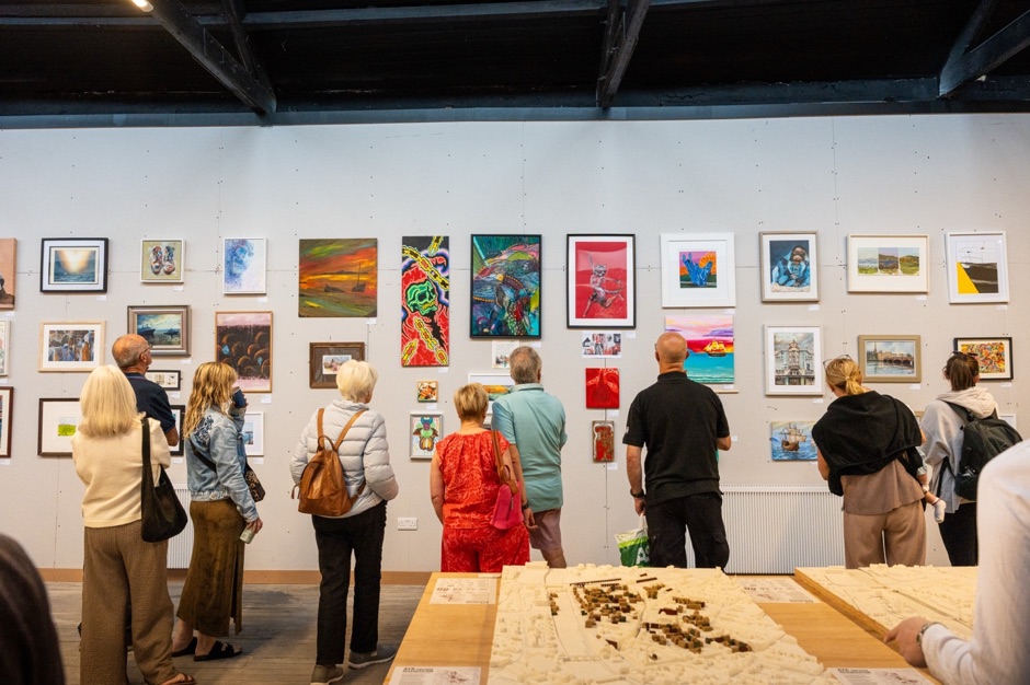 Visitors standing in front of a salon-style hang of artwork at the Ayr: Past, Present, Future exhibition