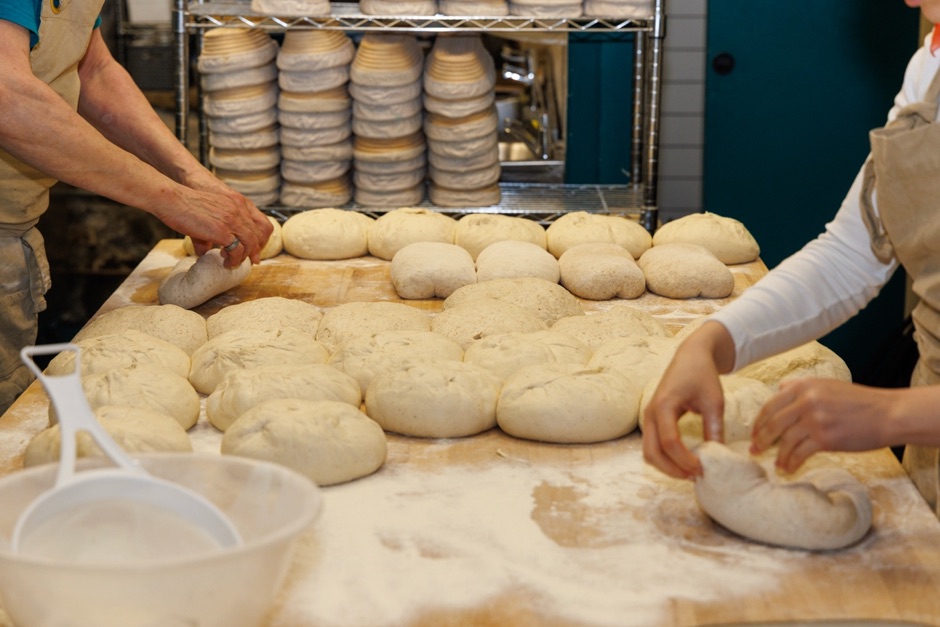 Two bakers shaping rounds of sourdough dough on a floured wooden bench at Narture's Knead bakery